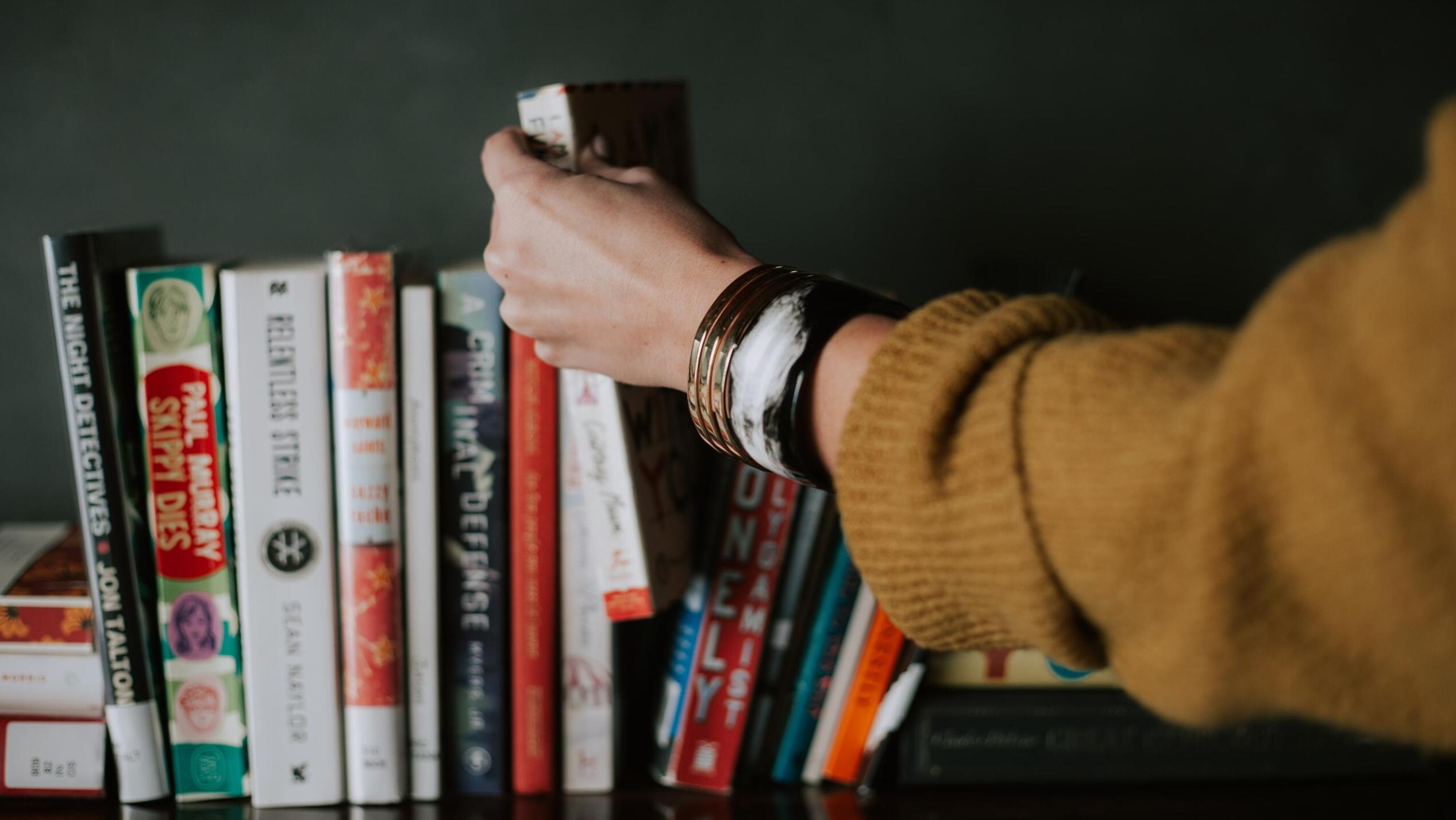 Eine Hand nimmt ein Buch aus einem Regal.