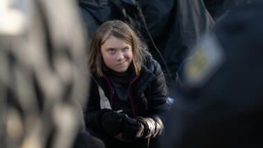 Greta Thunberg zwinkert in eine Kamera, um sie rum schemenhaft Polizisten