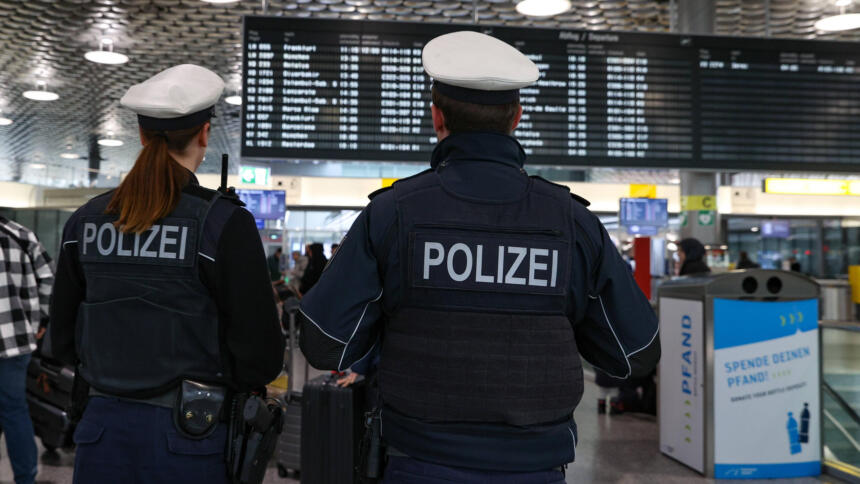 Zwei Polizisten von Hinten, im Hintergrund eine Flughafen-Tafel