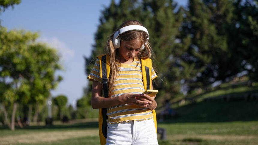 Teenagerin mit Kopfhörern schaut auf ihr Smartphone