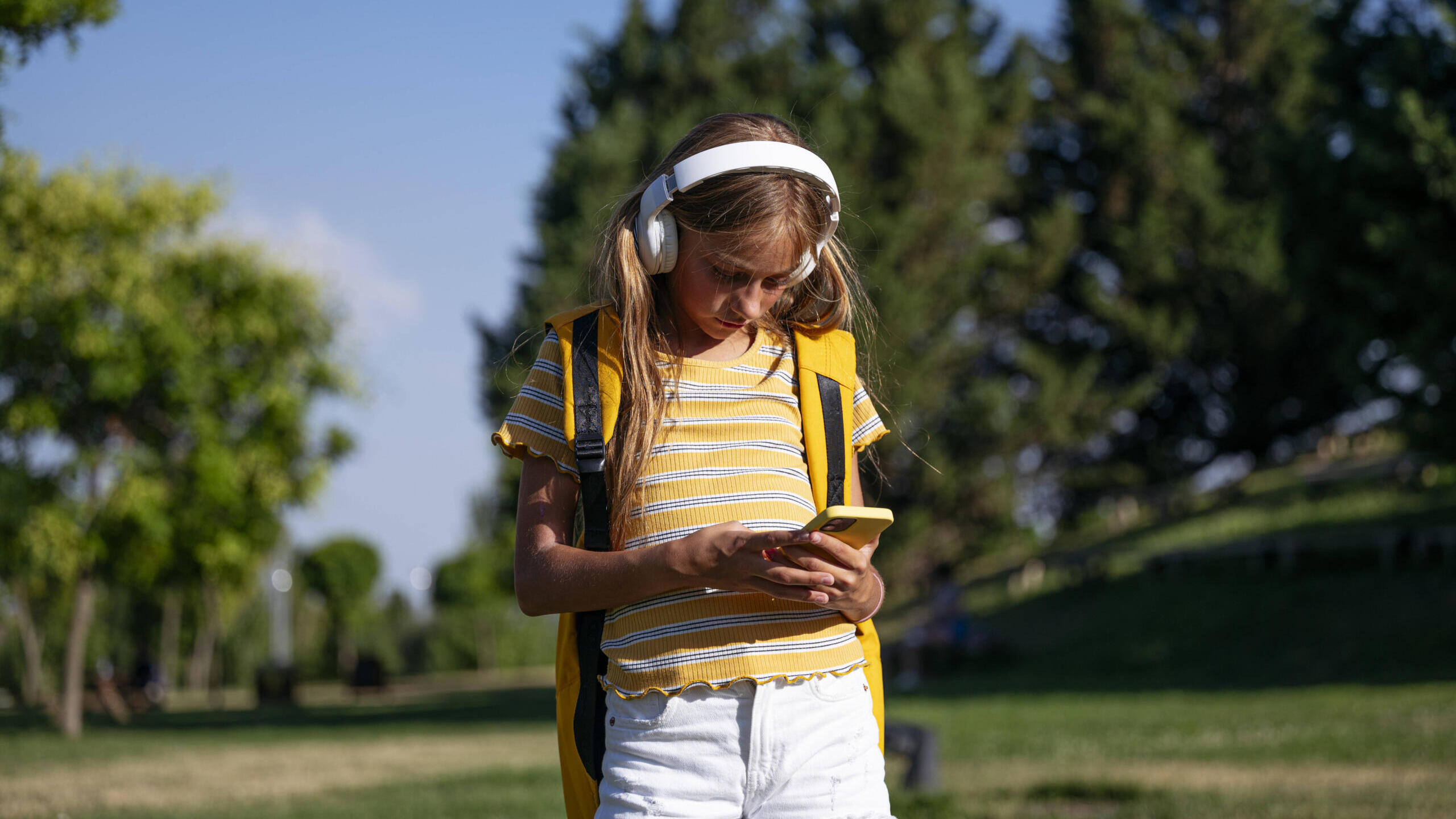 Teenagerin mit Kopfhörern schaut auf ihr Smartphone