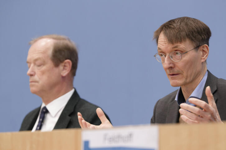 zwei weiße Männer im Anzug an einem Pult, der eine hebt die Hände beim Sprechen