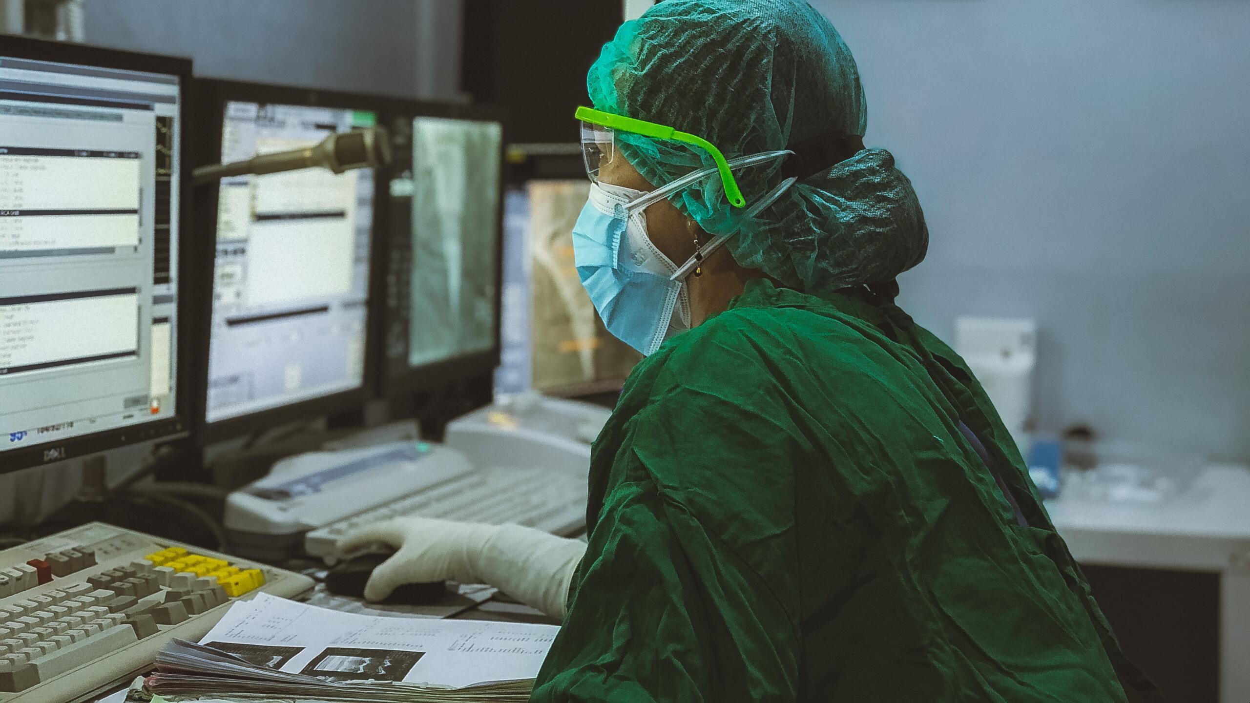 Eine Laborantin sitzt vor dem Computer in Schutzkleidung