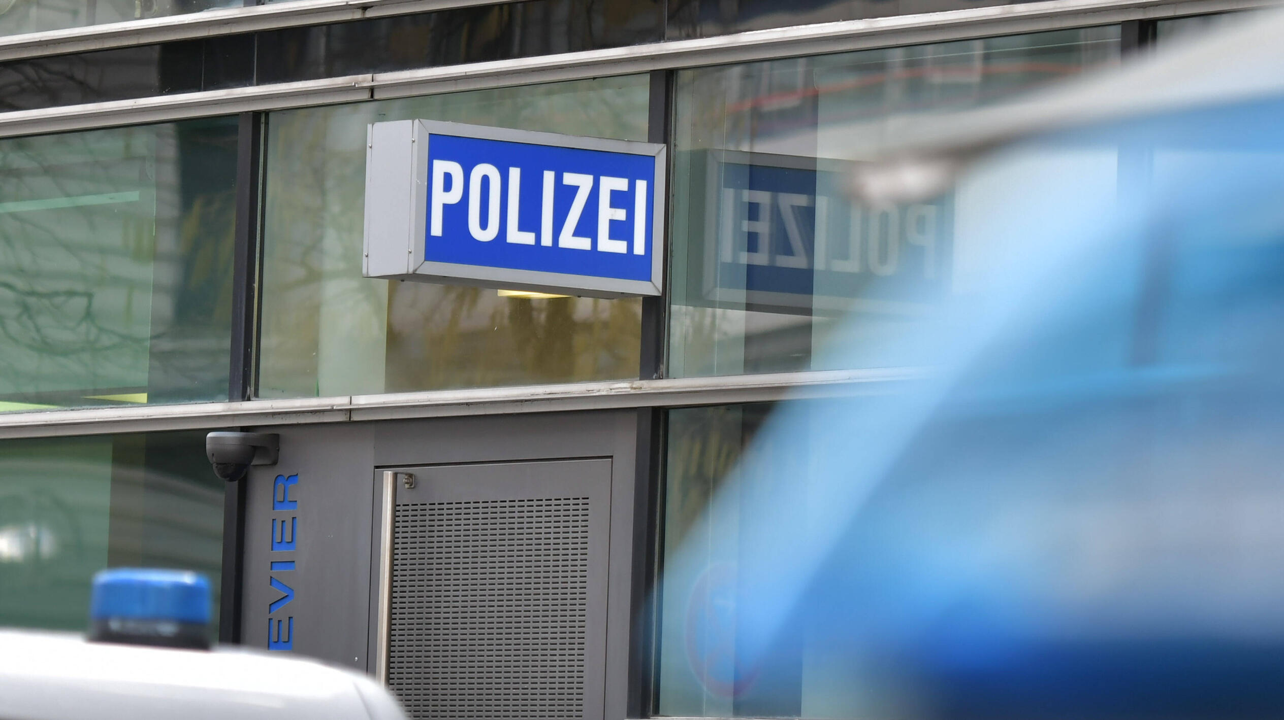 Eine gläsere Gebäudefasse mit einem großen, blauen Schild, auf dem in weißer Schrift "Polizei" steht
