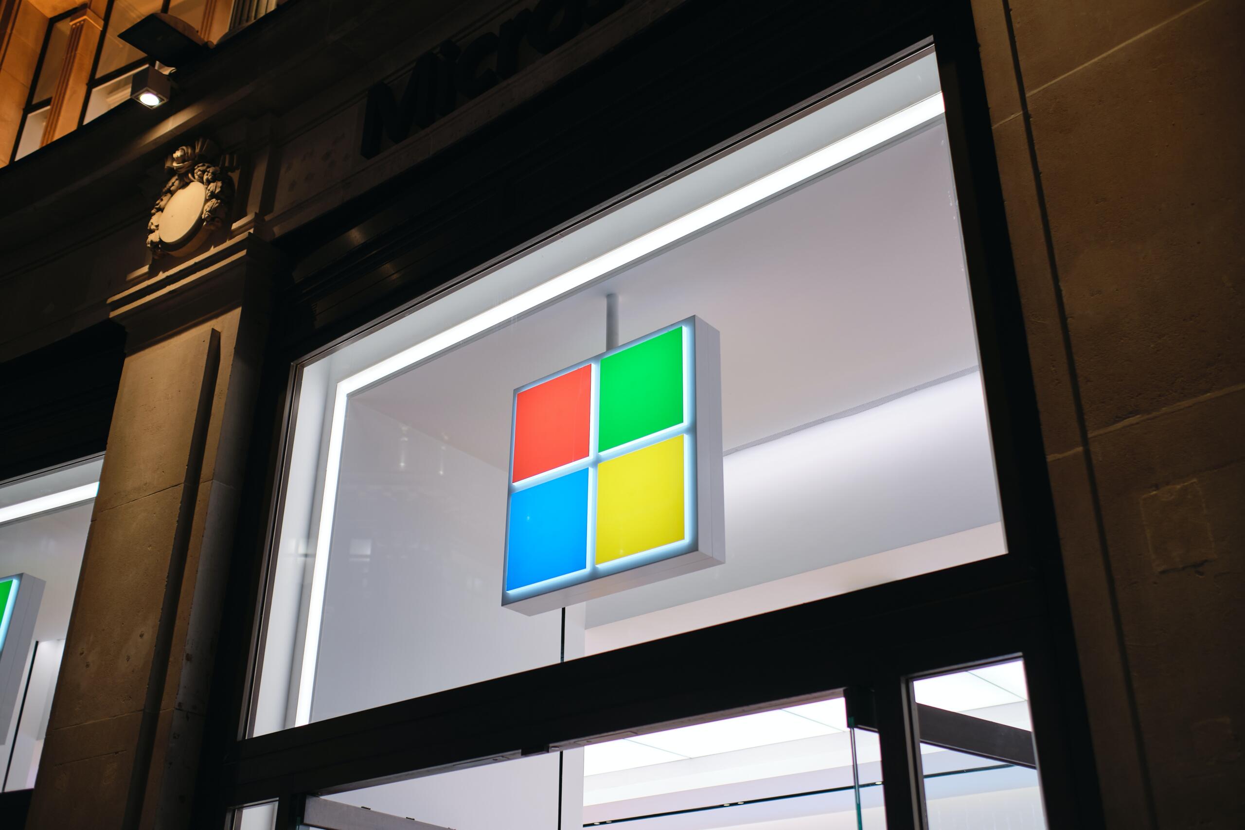 Das vierfarbige Firmenlogo von Microsoft erscheint über dem Eingang zu einem Microsoft-Store.