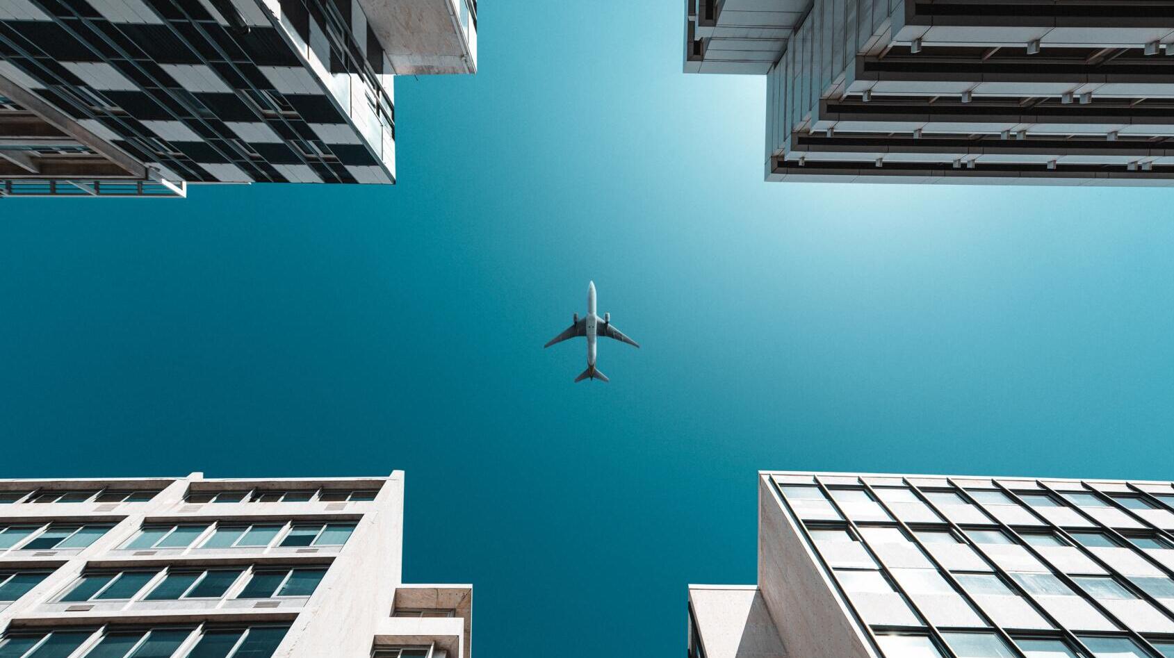 Ein Flugzeug, von unten zwischen vier Hochhäusern fotografiert