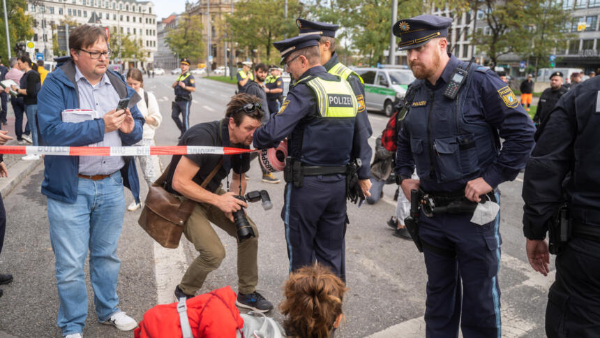 Polizist versucht Absperrband vor einen Fotografen zu ziehen.