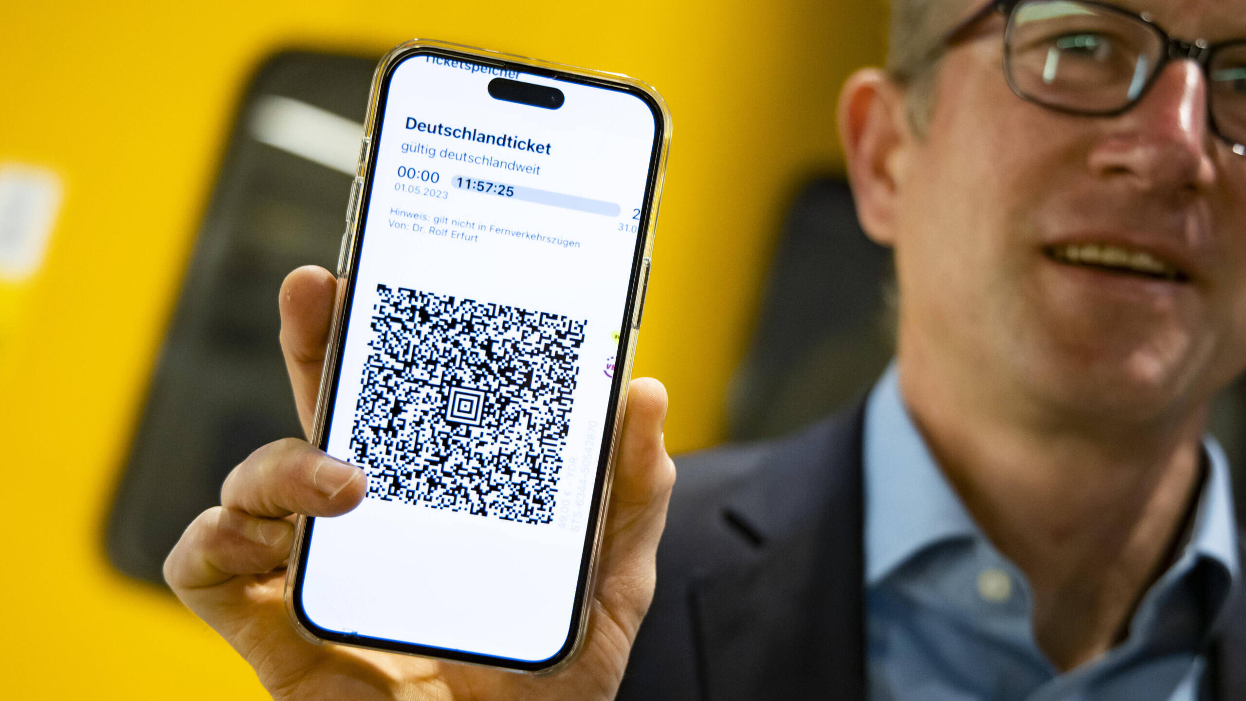 Mann hält Handy mit Deutschlandticket in die Kamera.