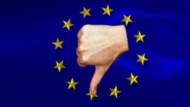 Eine weiße Hand vor dem Hintergrund der EU-Flagge, die einen Daumen nach unten zeigt