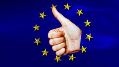 Eine weiße Hand vor dem Hintergrund der EU-Flagge, die einen Daumen nach oben zeigt