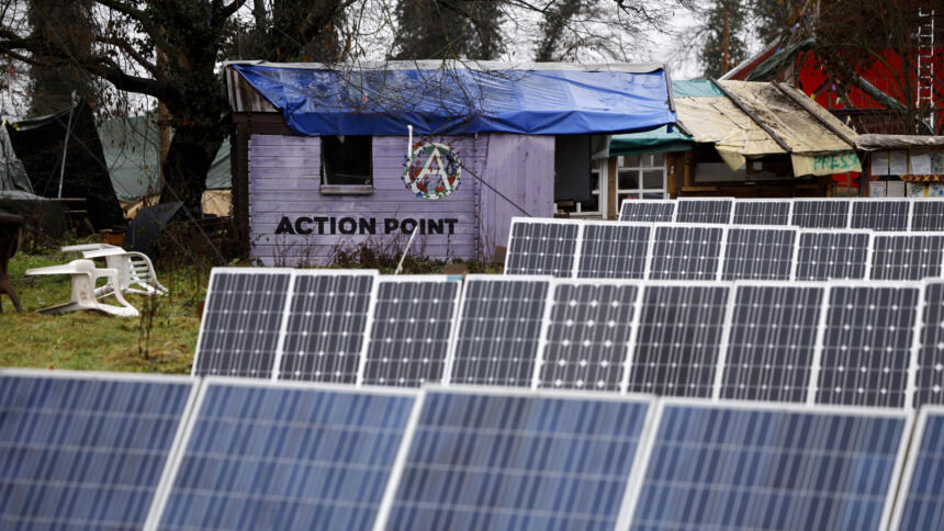 Im Vordergrund mehrere Reihen Solarzellen, im Hintergrund selbstgebaute Hütten mit der Aufschrift "Action Point" und "Presse"