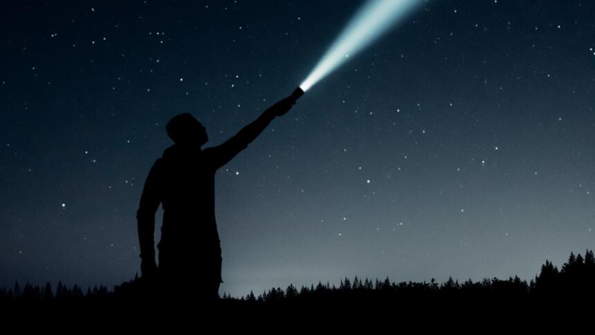 Ein Mensch strahlt mit einer Taschenlampe in den Nachthimmel