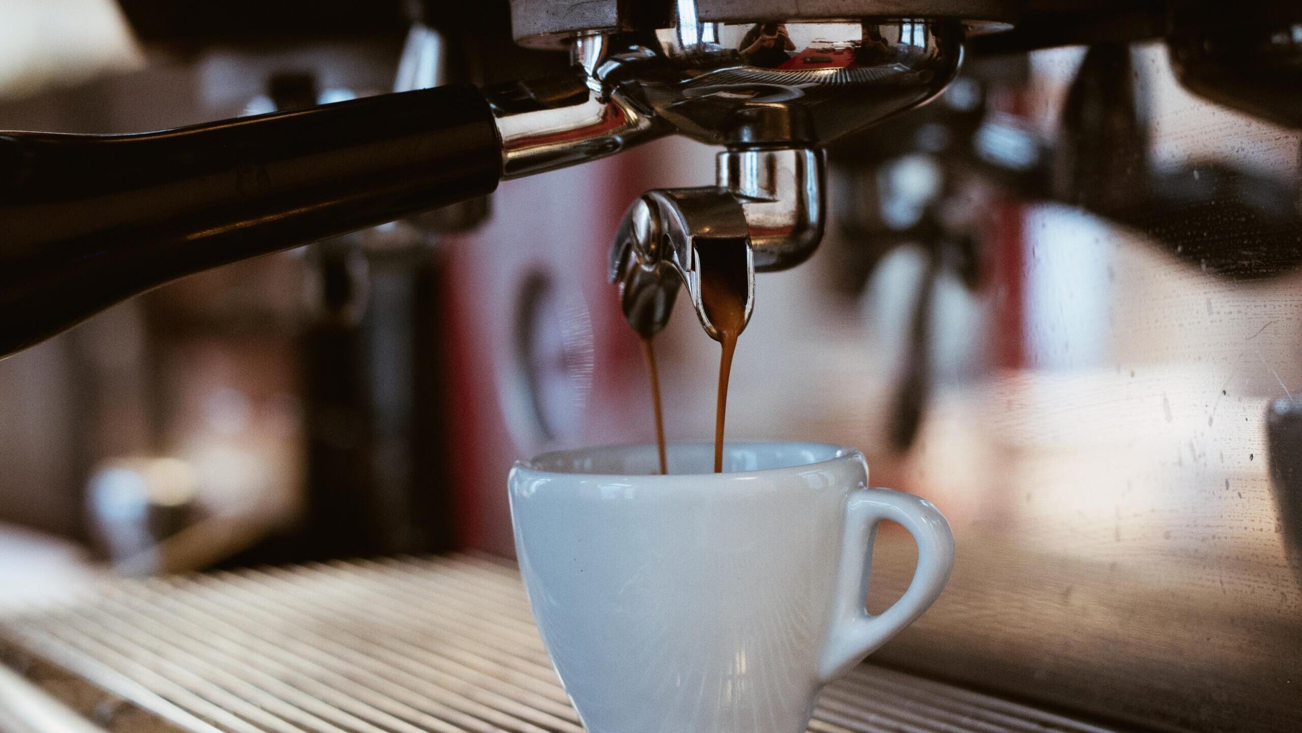 Nahaufnahme einer weißen Kaffeetasse unter einer laufenden Siebträgermaschine