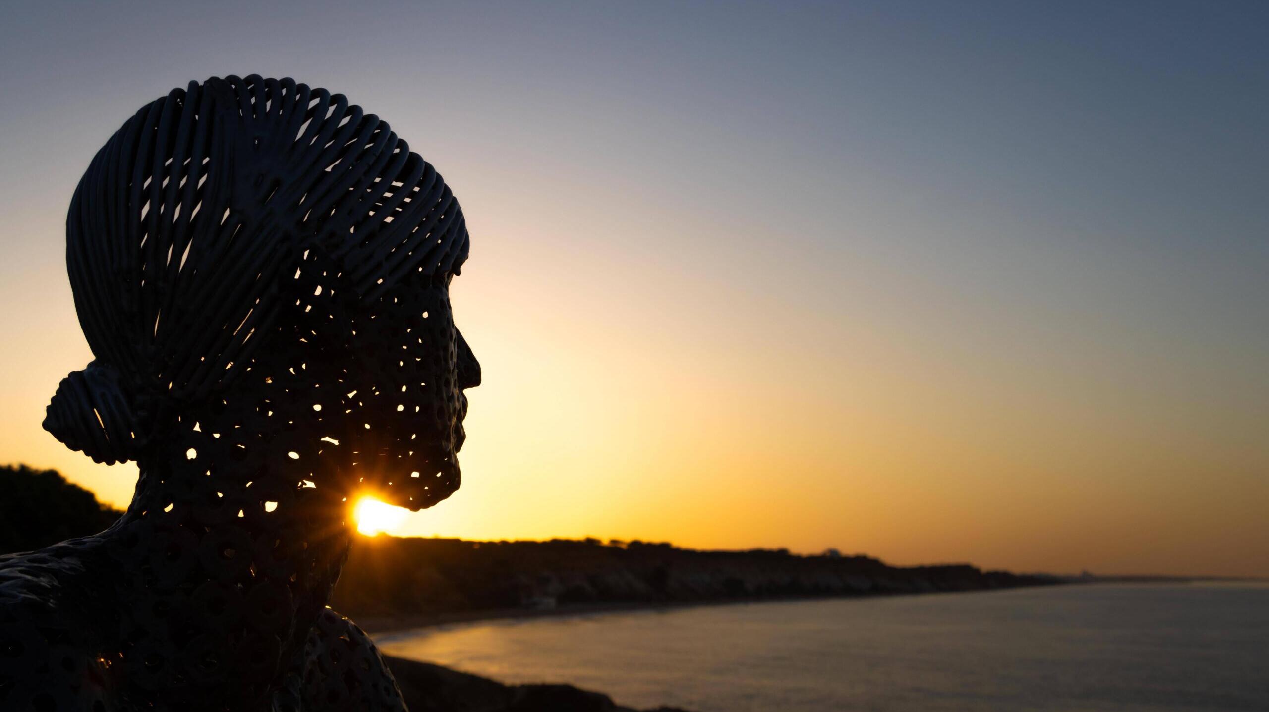 Eine Metall-Skulptur des Künstlers Carlos de Oliveira Correia blickt auf der Aussichtsplattform am Strand von Olhos des Augua bei Sonnenaufgang auf den Atlantik hinaus.