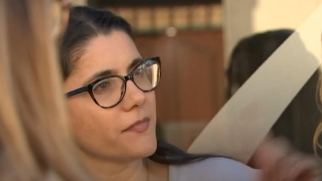 Frau mit dunkler Brille und langen dunklen Haaren schaut jemanden an, der nicht im Bild ist