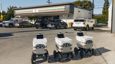 Drei Liefer-Roboter stehen vor einem Seven-Eleven-Laden.