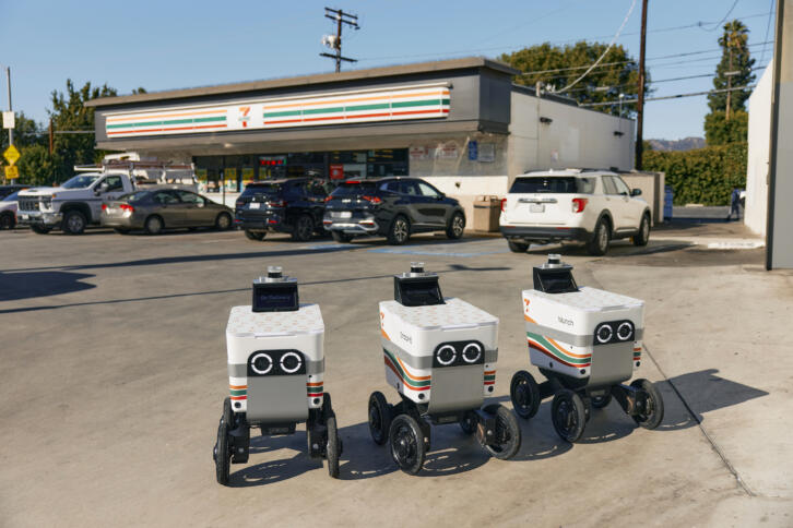 Drei Liefer-Roboter stehen vor einem Seven-Eleven-Laden.