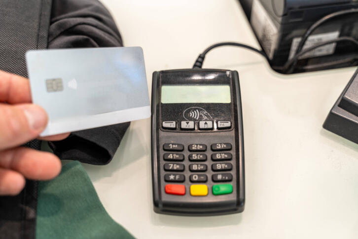 Eine Beazhlkarte wird an ein EC-Kartenlesegerät auf einem Tisch gehalten.