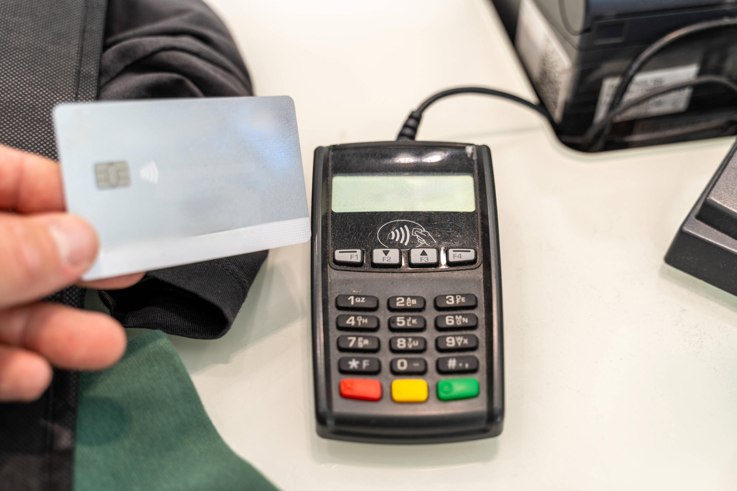Eine Beazhlkarte wird an ein EC-Kartenlesegerät auf einem Tisch gehalten.