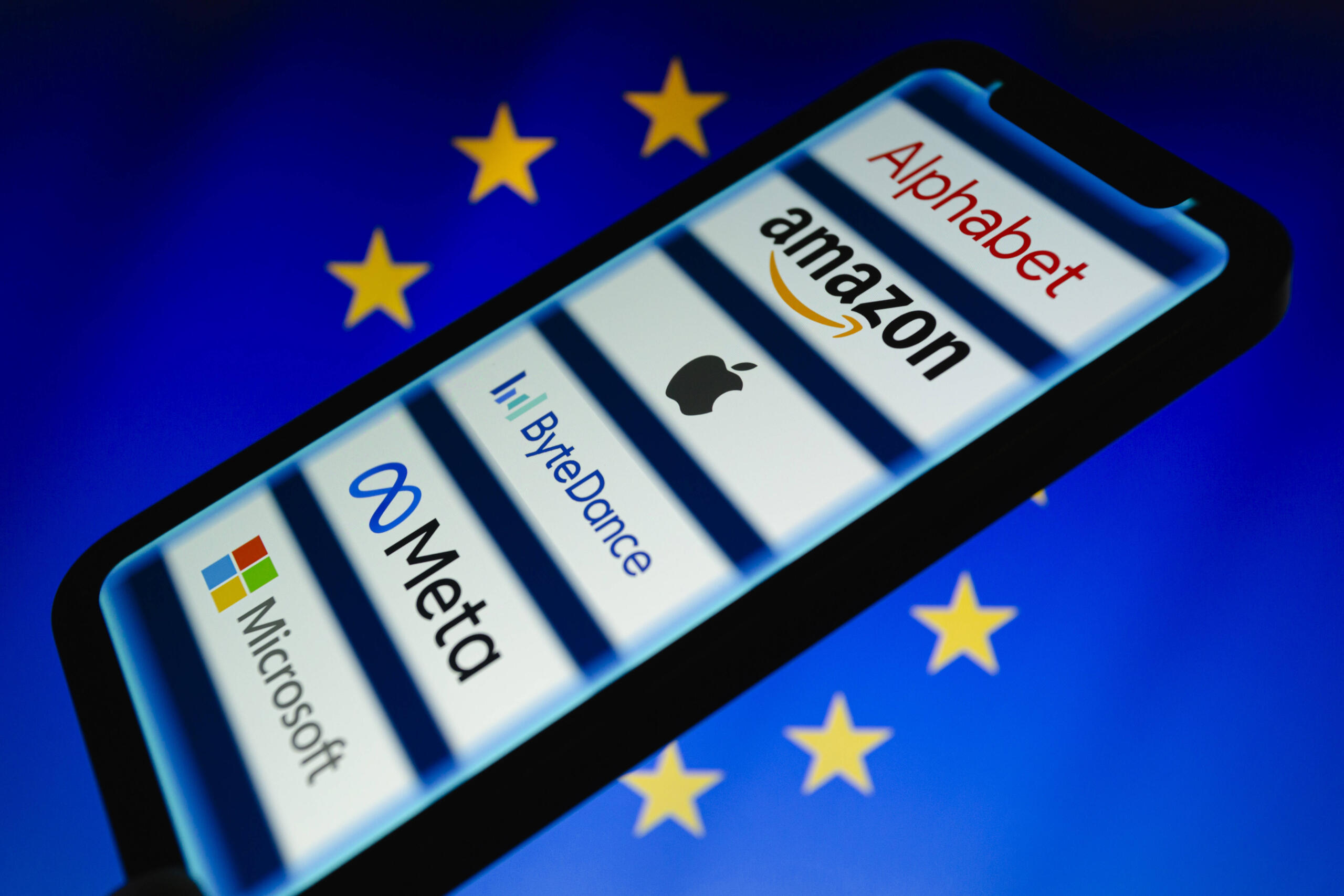Ein Smartphone, auf dem die Logos von Alphabet, Amazon, Apple, ByteDance, Meta und Microsoft zu sehen sind. Im Hintergrund ist die Flagge der Europäischen Union zu sehen.