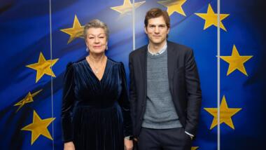 Ylva Johansson und Ashton Kutcher vor Europafahne