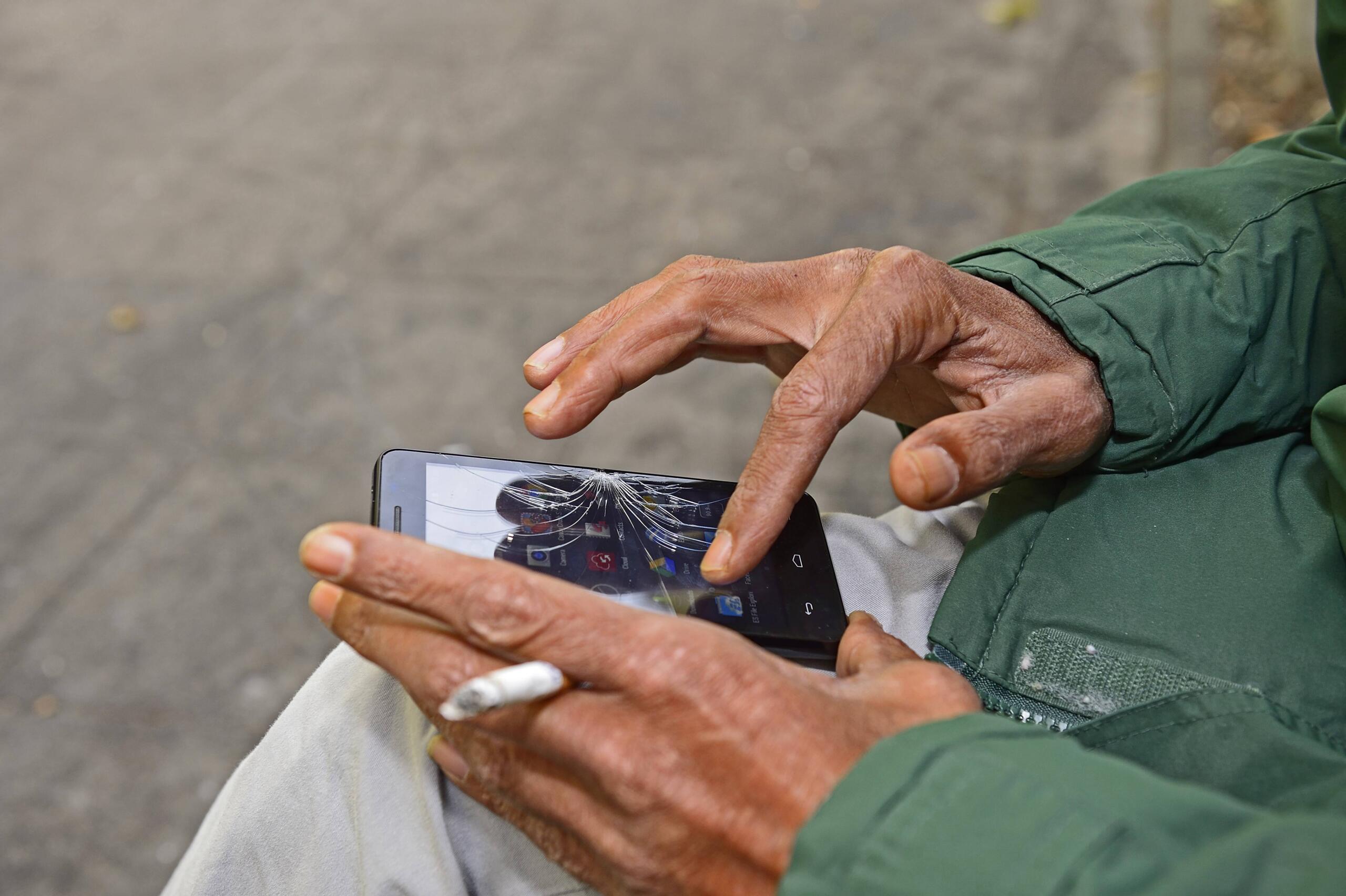 Ein Mann tippt auf einem Smartphone mit gesprungenem Display.