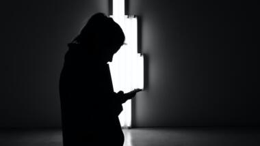 Eine Frau im Dunkeln schaut auf ihr Smartphone, im Hintergrund ein helles, weißes Licht