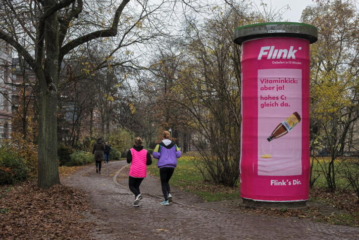 Zwei Joggerinnen laufen an einer Litfaßsäule mit Flink-Werbung vorbei