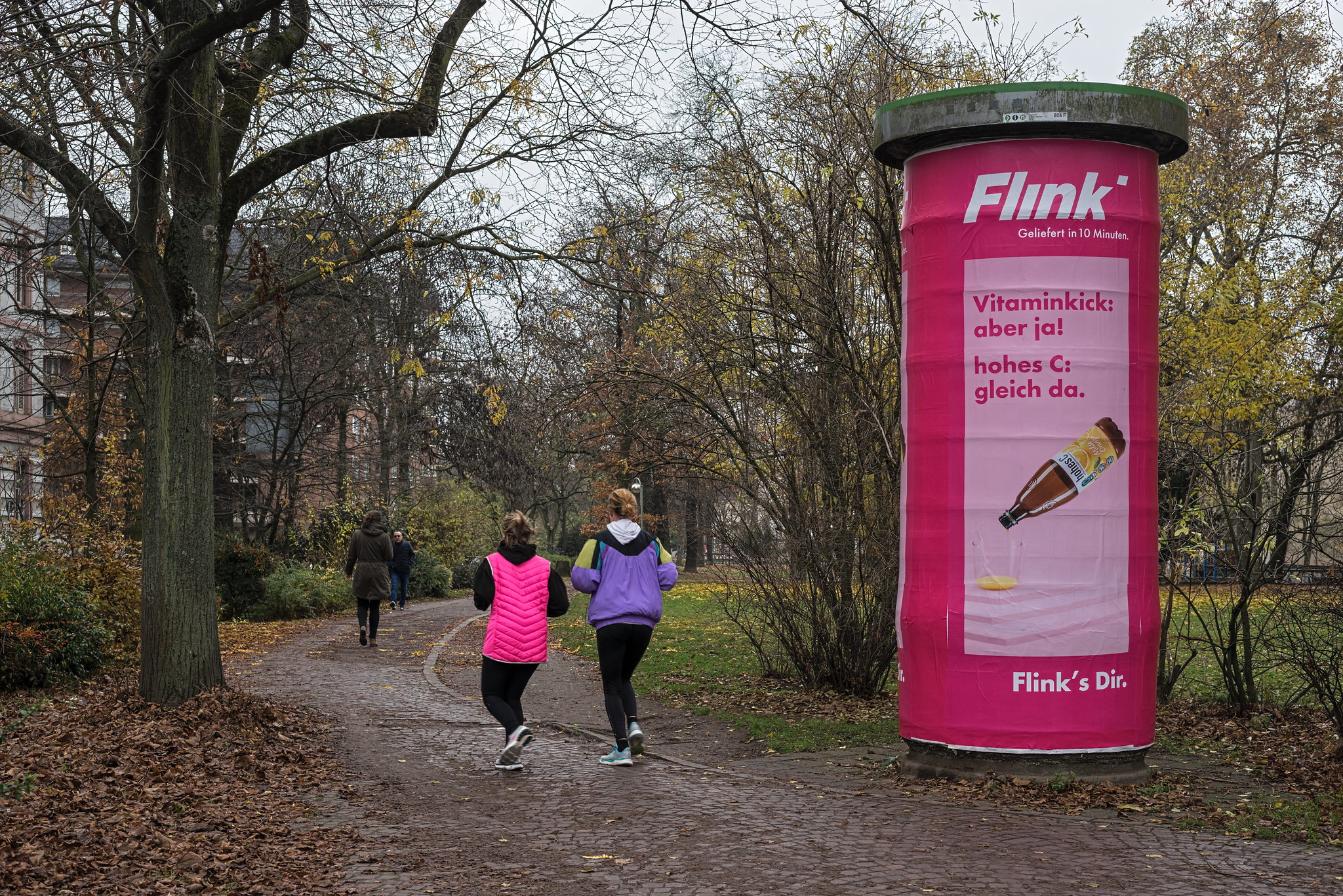 Zwei Joggerinnen laufen an einer Litfaßsäule mit Flink-Werbung vorbei