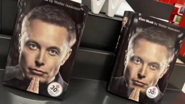 Zwei Bücher, auf denen Elon Musk mit gefalteten Händen zu sehen ist.
