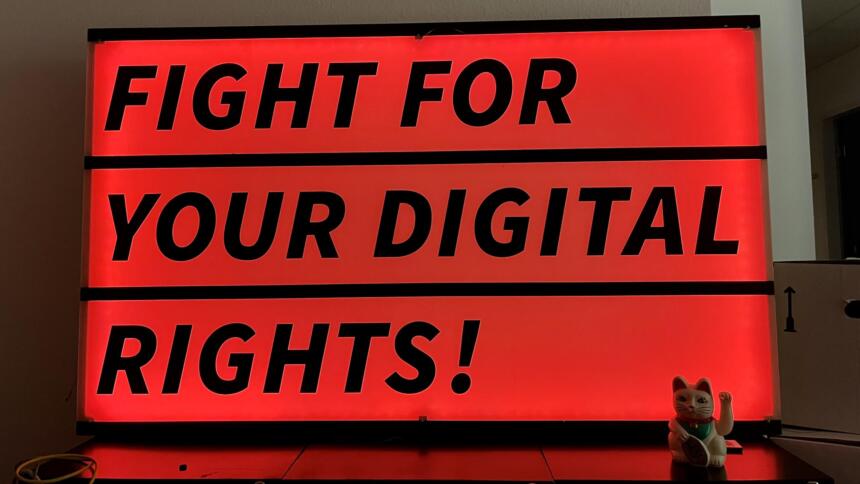 Eine Leuchtreklame in rot mit dem Schriftzug "We fight for your digital rights", im Hintergrund Umzugskisten