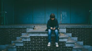 Ein Kind sitzt auf einer Treppe und schaut mit gesenktem Kopf in sein Smartphone