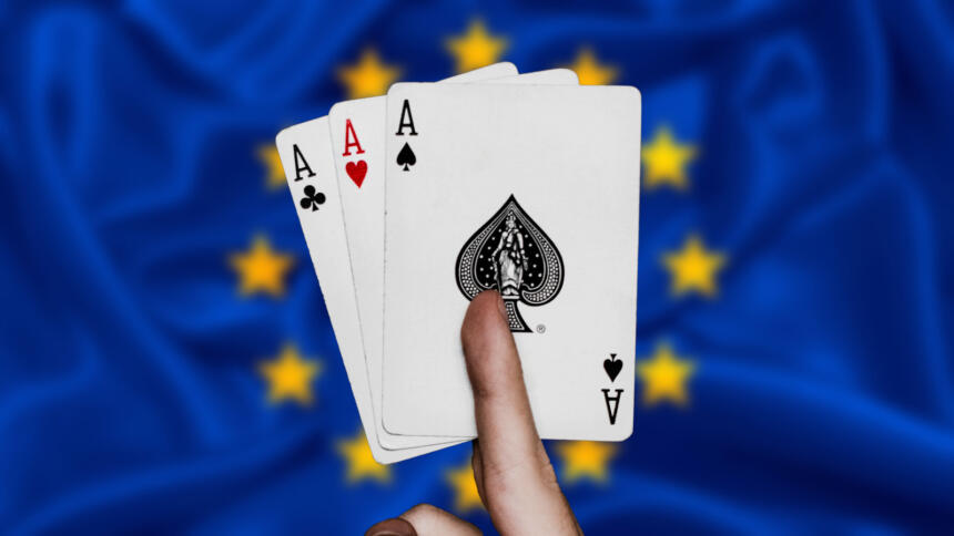 Eine Hand hält einen Stich mit drei Assen, im Hintergrund die Flagge der EU