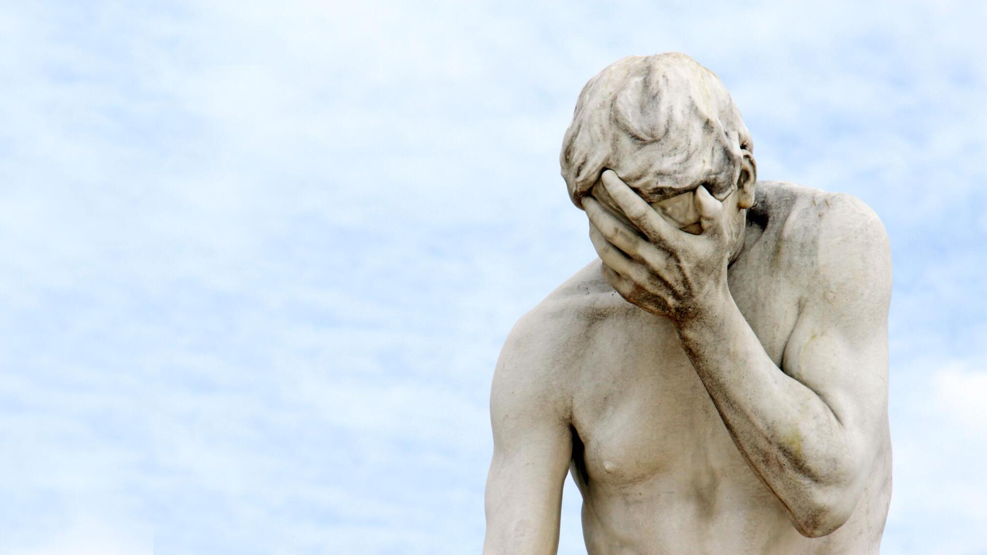 Statue vor Wolkenhimmel hält sich die Hand auf die Stirn