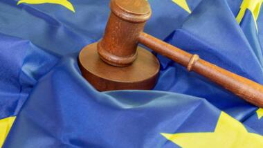 Ein Richterhammer und ein Resonanzblock aus Holz auf einer Flagge der Europäischen Union.