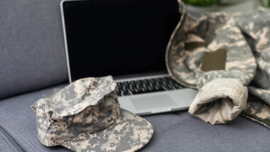 Ein Laptopn, davor eine Militärmütze in Camouflage und dahinter eine Jacke in Camouflage