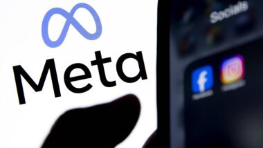 EinSmartphone auf dem Icons von Facebook und Instagram sichtbar sind, vor einem hellen Banner mit dem Meta-Logo.