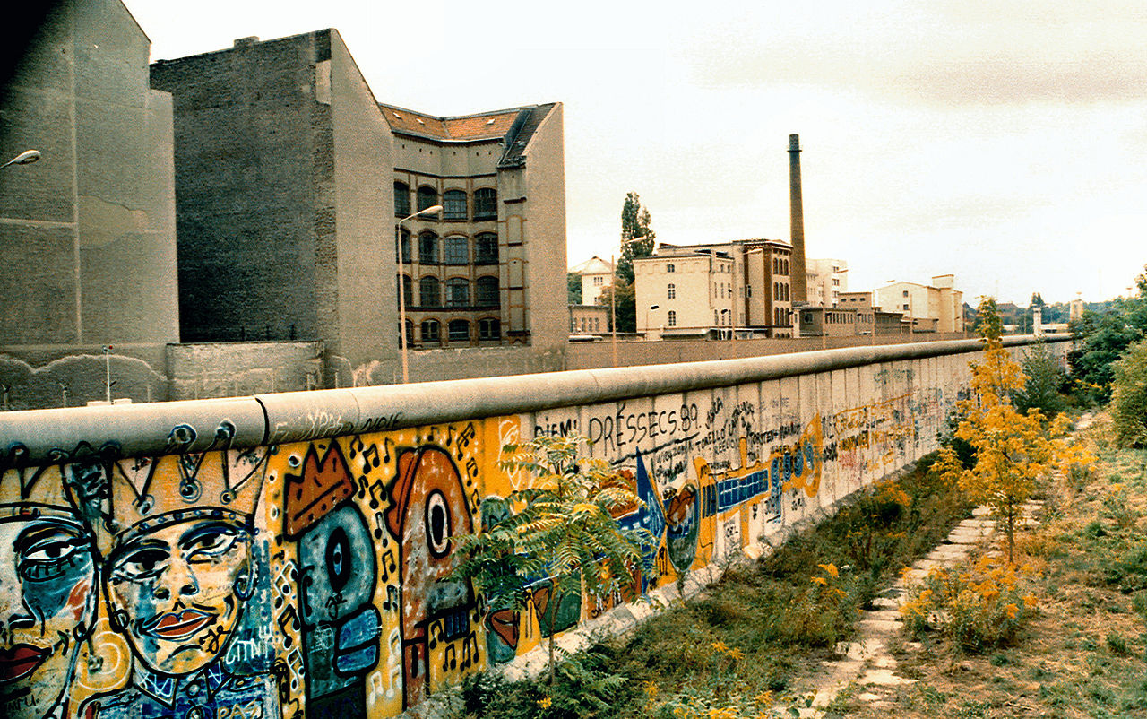 Die frühere Berliner Mauer, dahinter Gebäude, davor ein Grünstreifen
