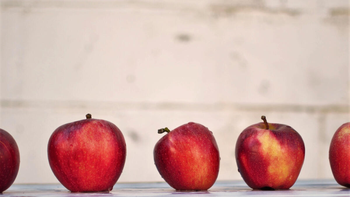 eine Reihe roter Äpfel vor einer hellen Mauer