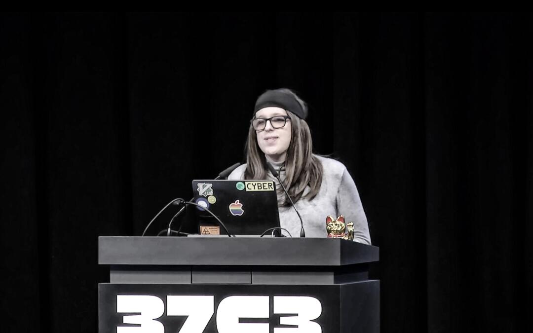 Casey Kreer steht am Pult, auf dem eine Winkekatze steht sowie die Aufschrift "37C3"