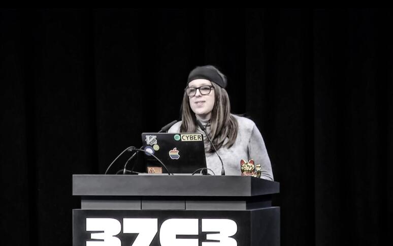 Casey Kreer steht am Pult, auf dem eine Winkekatze steht sowie die Aufschrift "37C3"