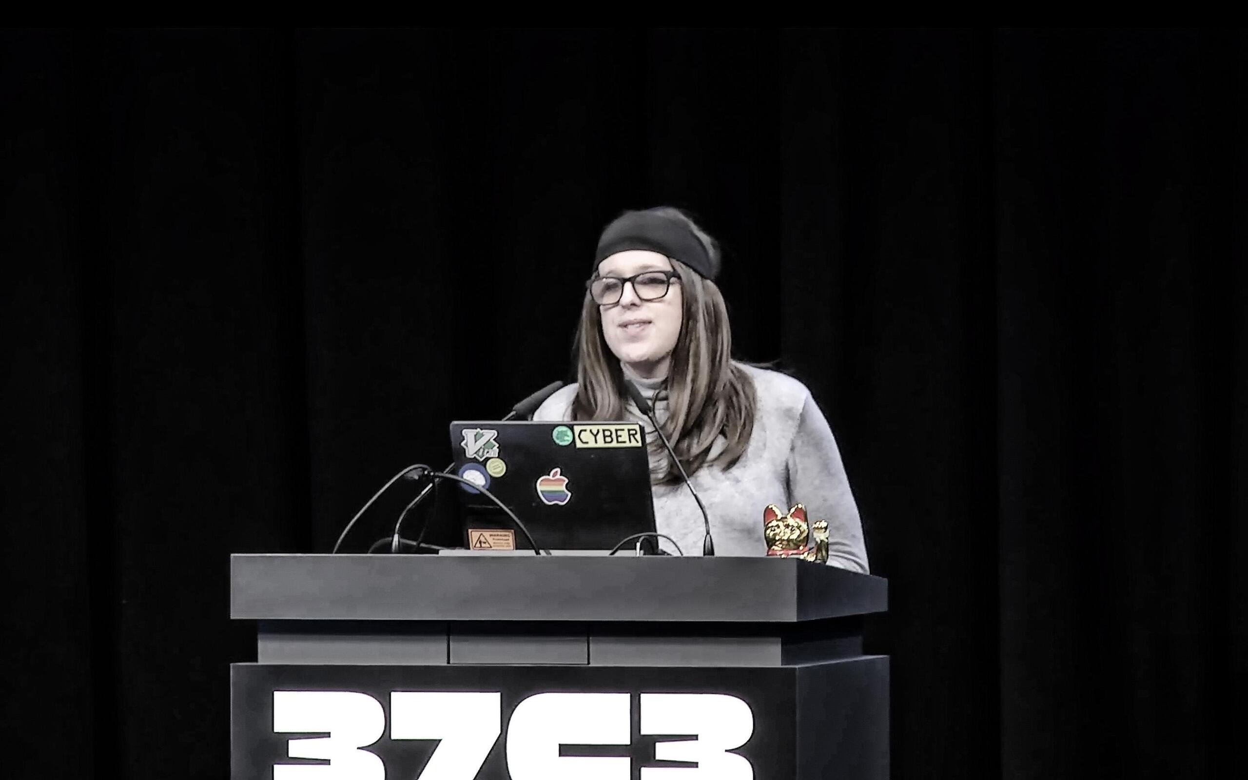 Casey Kreer steht am Pult, auf dem eine Winkekatze steht sowie die Aufschrift "37C3"