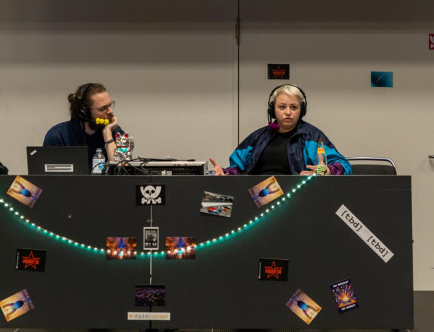 Ein Mann und eine Frau sitzen auf einem Podium und nehmen einen Podcast auf.