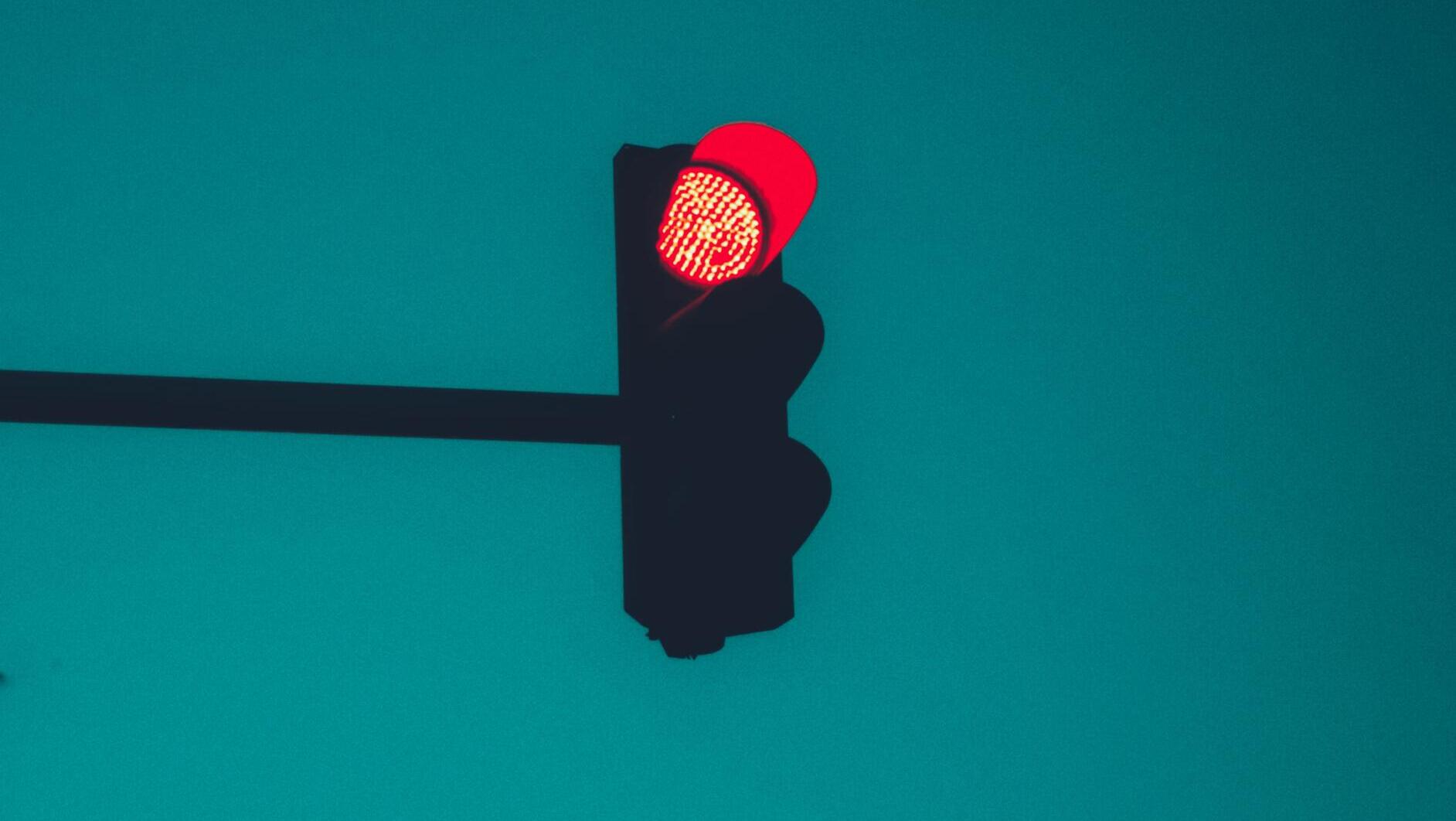 A red traffic light, with a blue sky in the background.