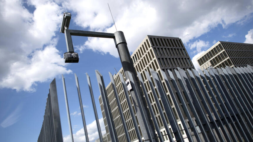Ein Metallzaun mit Überwachungskamera, dahinter das Gebäude des BND
