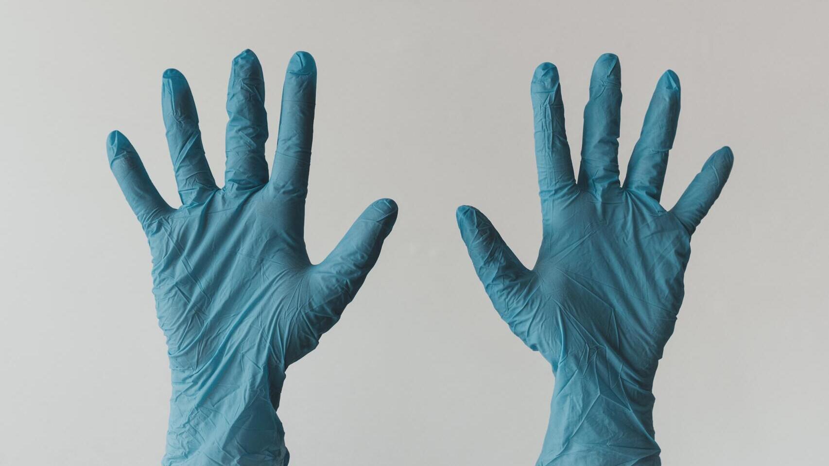 Zwei erhobene Hände in Latex-Handschuhen