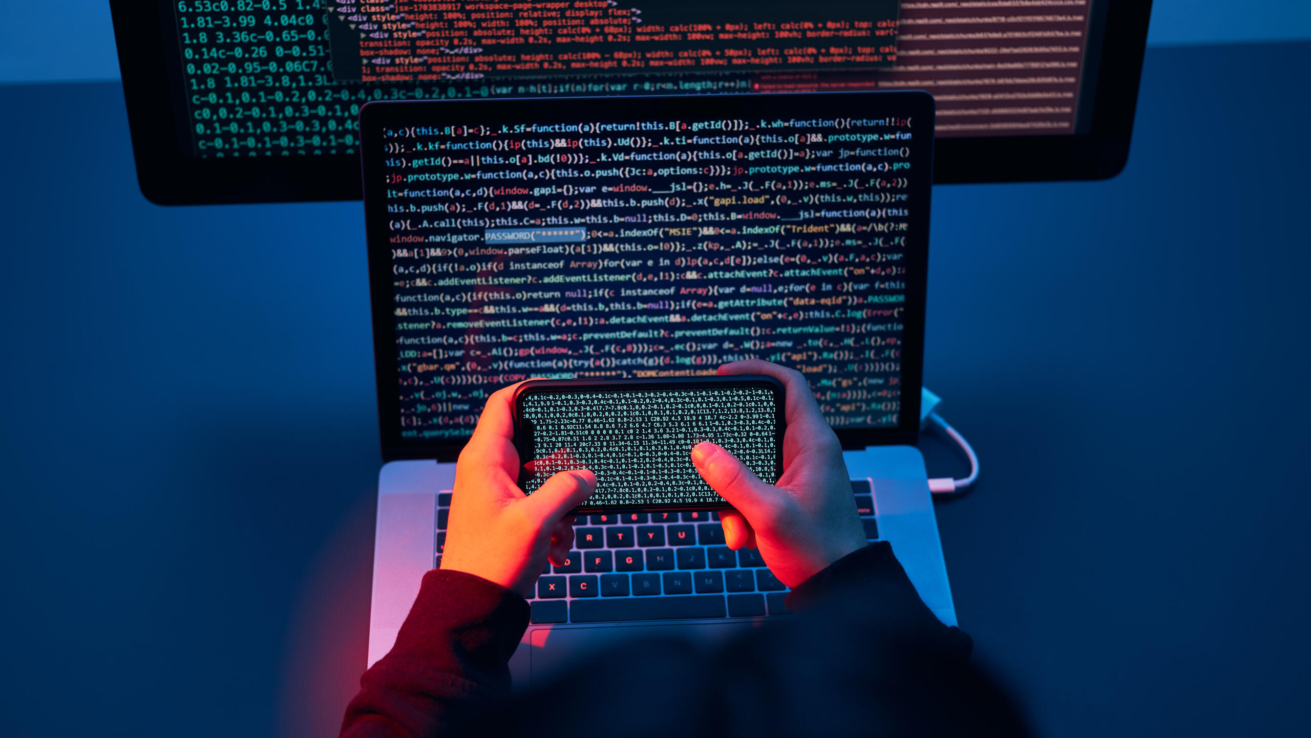 Hacker hält ein Handy vor einem Bildschirm, der vor einem Bildschirm ist.