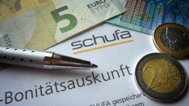 Schufa-Zettel mit Bonitätsauskunft, ein Kugelschreiber und Münzen