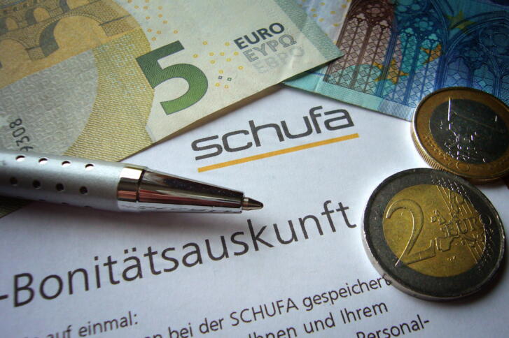 Schufa-Zettel mit Bonitätsauskunft, ein Kugelschreiber und Münzen