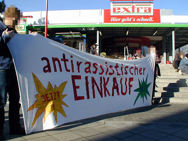 Transparent auf einer Demo vor einem Supermarkt mit der Aufschrift "antirassistischer Einkauf jetzt"